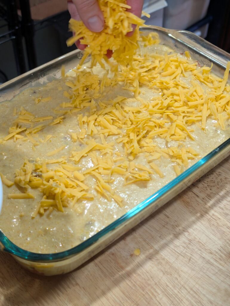 Hand sprinkling grated cheese over a glass baking dish.