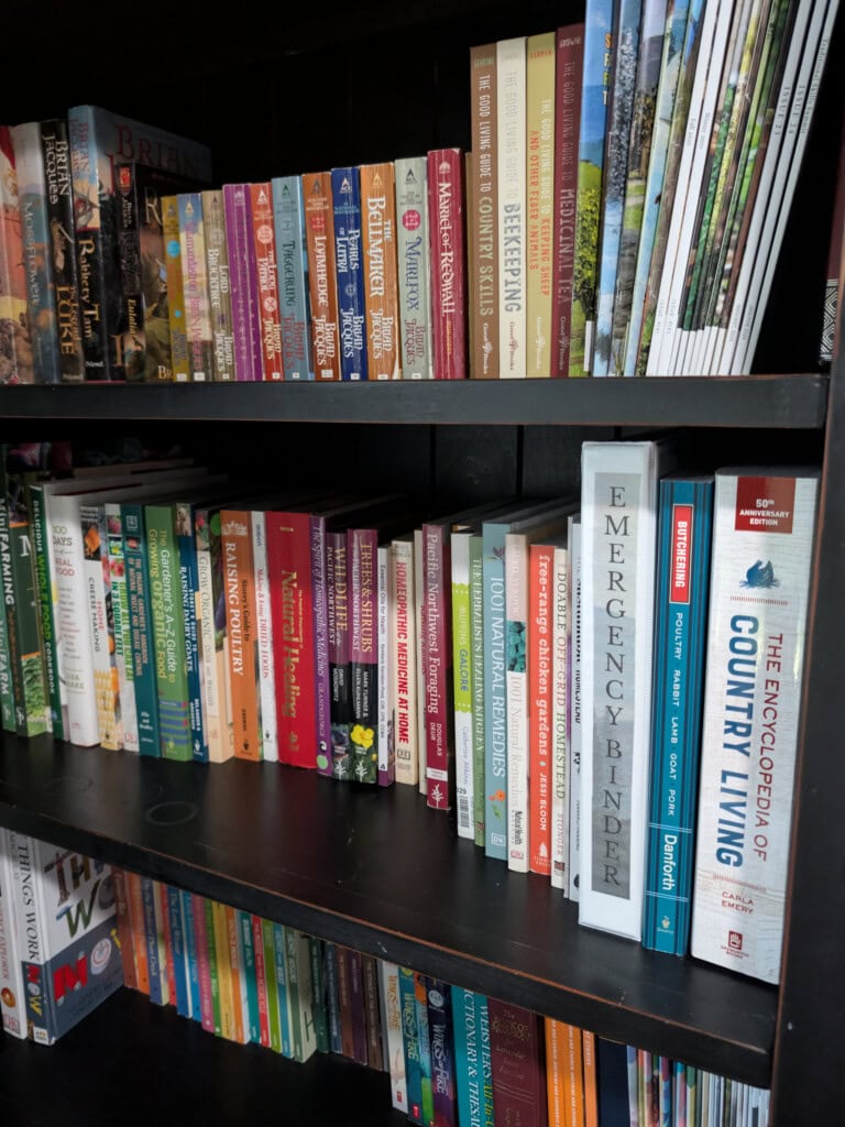 A white emergency binder sitting on a bookshelf next to homesteading and self-reliance books.