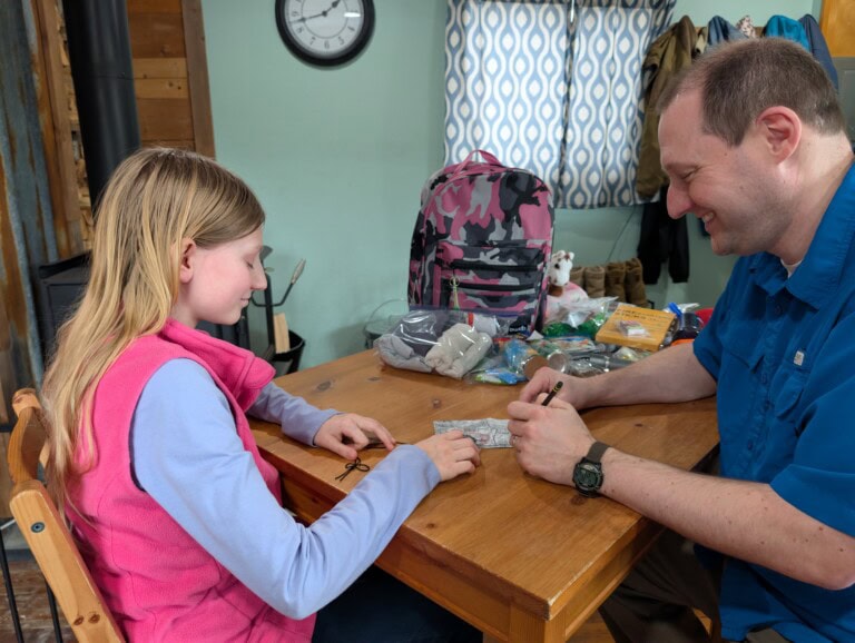 Dad teaching daughter a family preparedness plan using a map and emergency supplies.