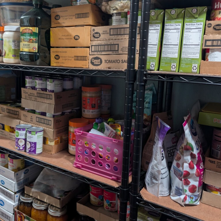 Well-stocked pantry shelves with organized cans, bulk staples, and home-canned jars, showing practical food storage for a self-sufficient kitchen.
