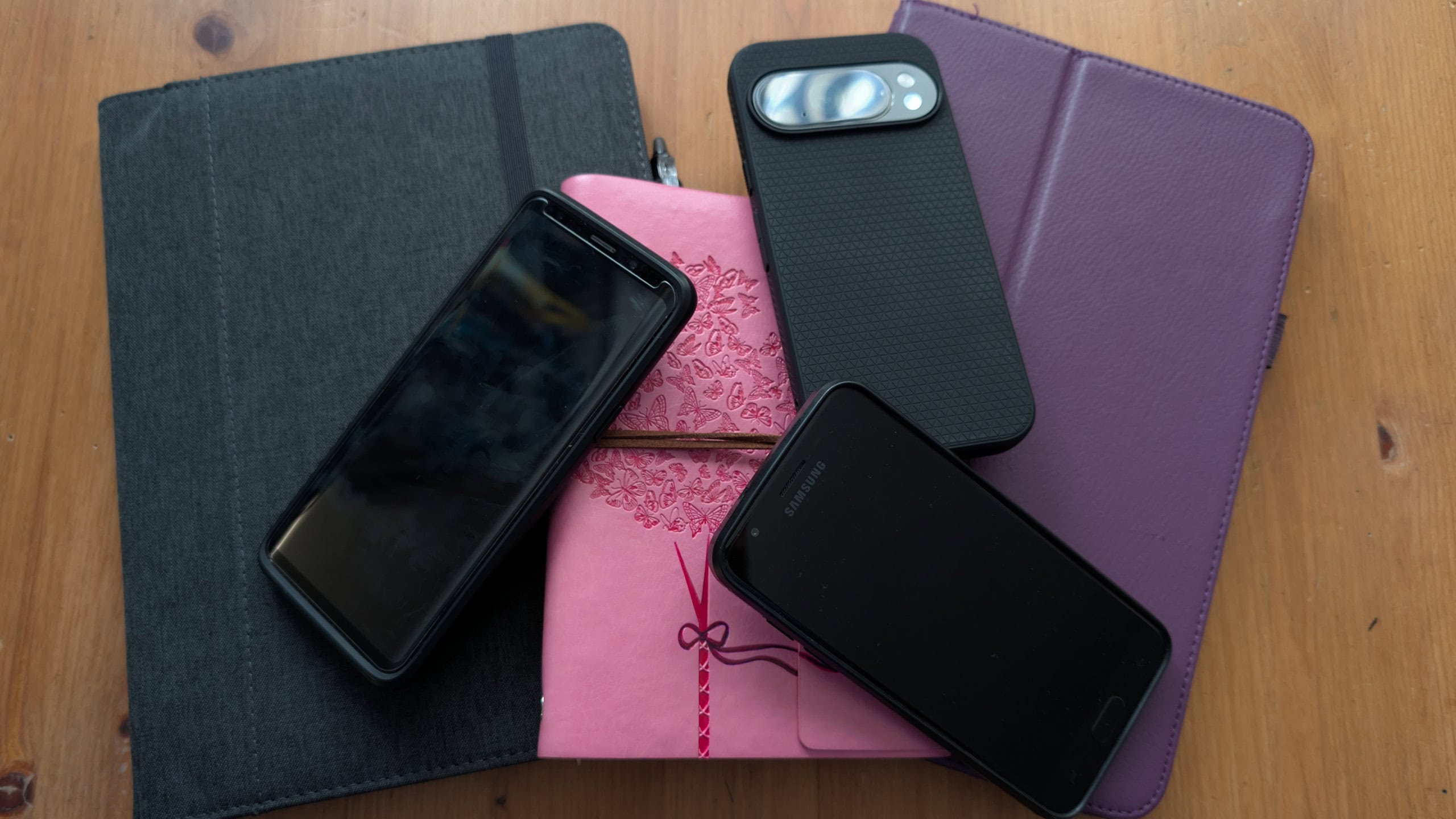 Pile of journals, phones, and tablets on a wooden table