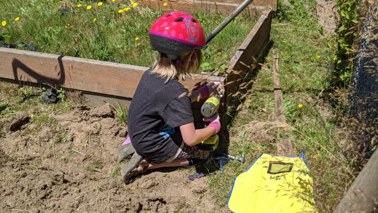 Young girl with drill working on garden bed outside