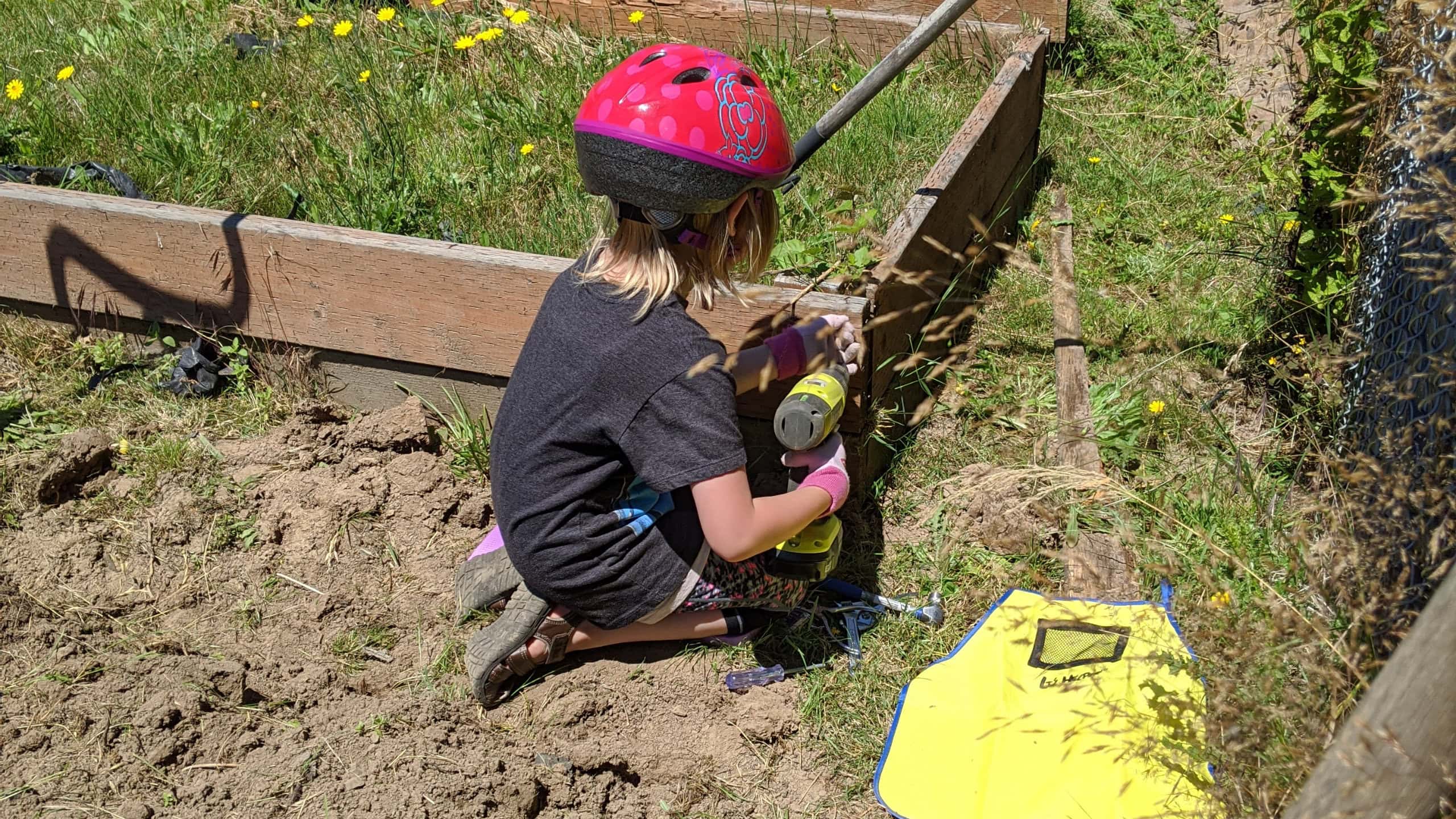 Young girl with drill working on garden bed outside
