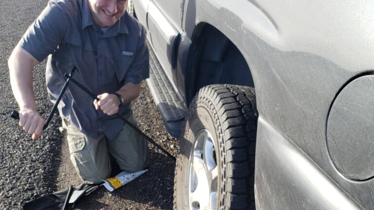 Man working jack under vehicle to change flat tire