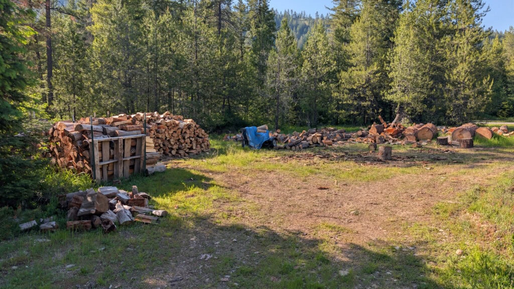 Logs and split wood with wood splitter in foreground, treeline in background